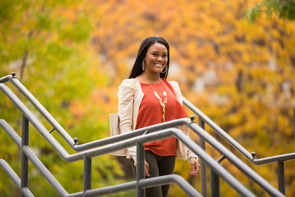 A student standing on stairs in fall foliage